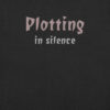Gothic-style text design reading “Plotting in Silence” in bold, moody font on a black t-shirt.