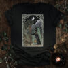 Illustration for the Hermit tarot cat t-shirt: a cloaked black cat holding a lantern and staff, standing near a barren tree with a book underneath, against a mountain backdrop and crescent moon. Text reads: “Only when utterly alone do you realize that you never are.”