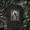 Black Cat in Autumn Graveyard T-shirt featuring a black cat perched on a gravestone, surrounded by falling autumn leaves, ivy, and mushrooms, capturing a quiet, darkly humorous vibe.