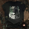 Saturn horsetail cat t-shirt featuring a black cat, a skull with growing horsetail, spring shoots, and Saturn in a hand-drawn botanical illustration.